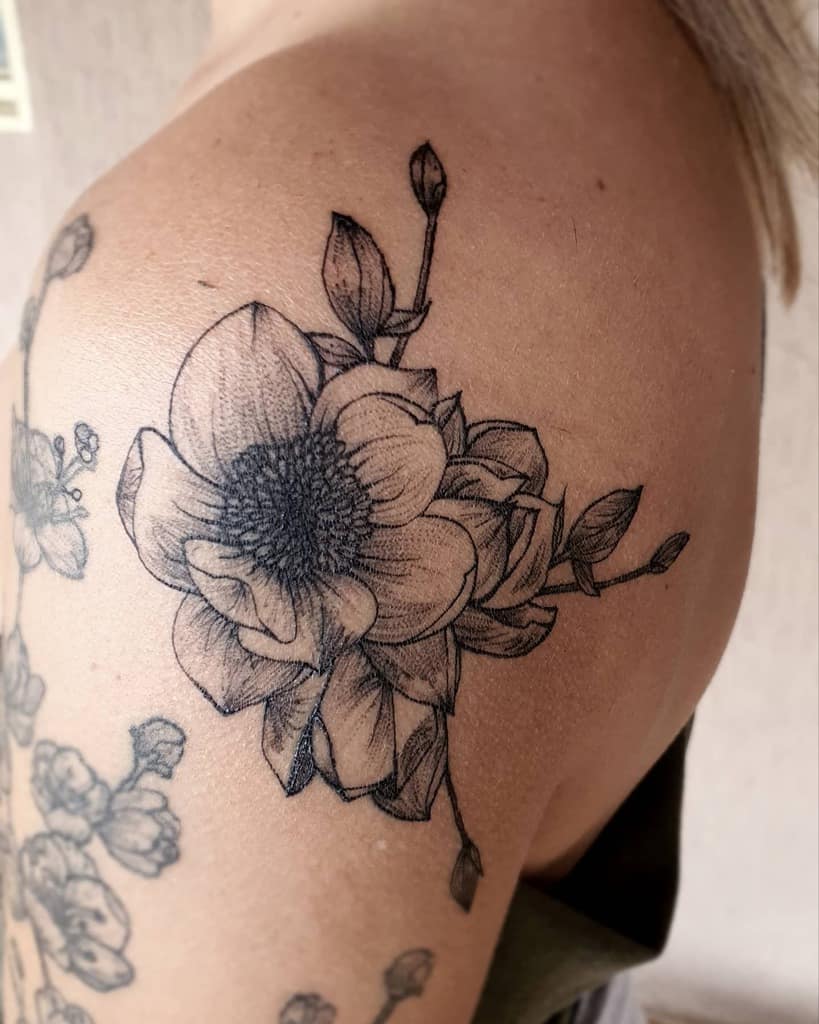 A stunning black and white magnolia floral tattoo graces a woman's upper arm, showcasing intricate details and timeless elegance