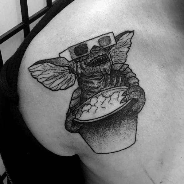 Black and gray Gremlin tattoo with 3D glasses and a bucket of popcorn, capturing a mischievous movie-night vibe in a bold design.