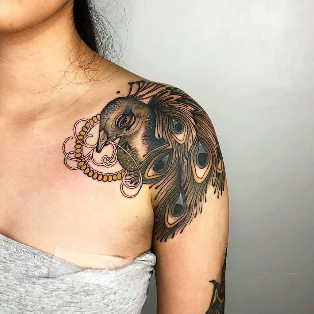 Peacock tattoo with intricate feather details and soft shading, framed with delicate circular patterns on the shoulder.