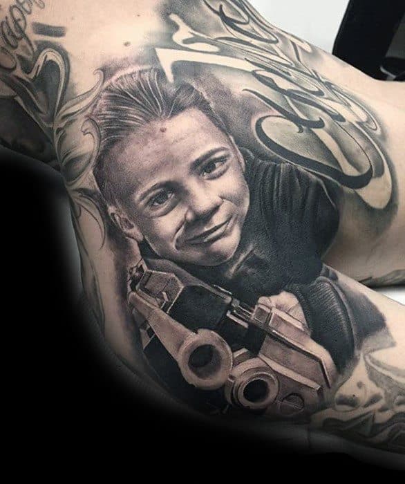 Tattoo of a smiling child holding a toy gun, surrounded by artistic designs
