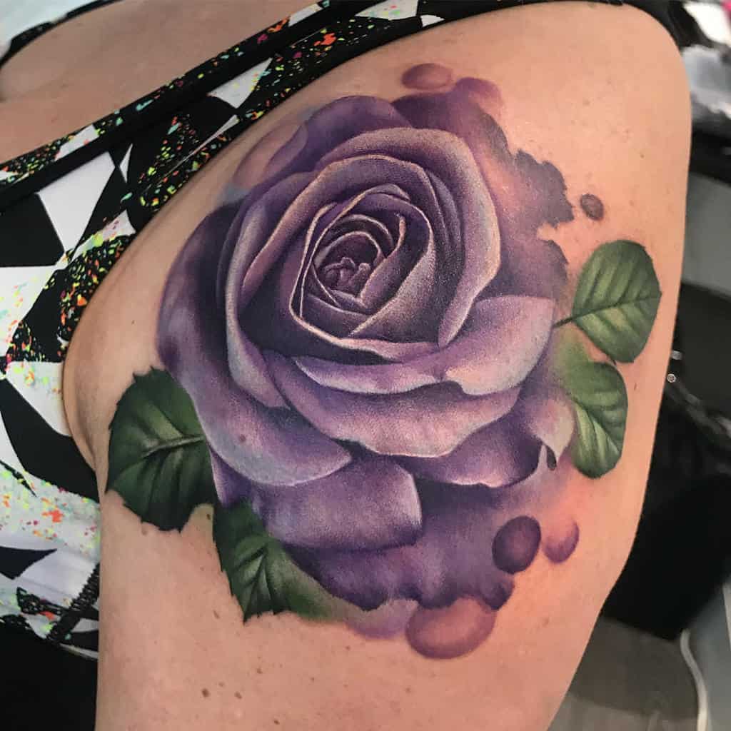 A realistic purple rose tattoo with green leaves on a woman's shoulder