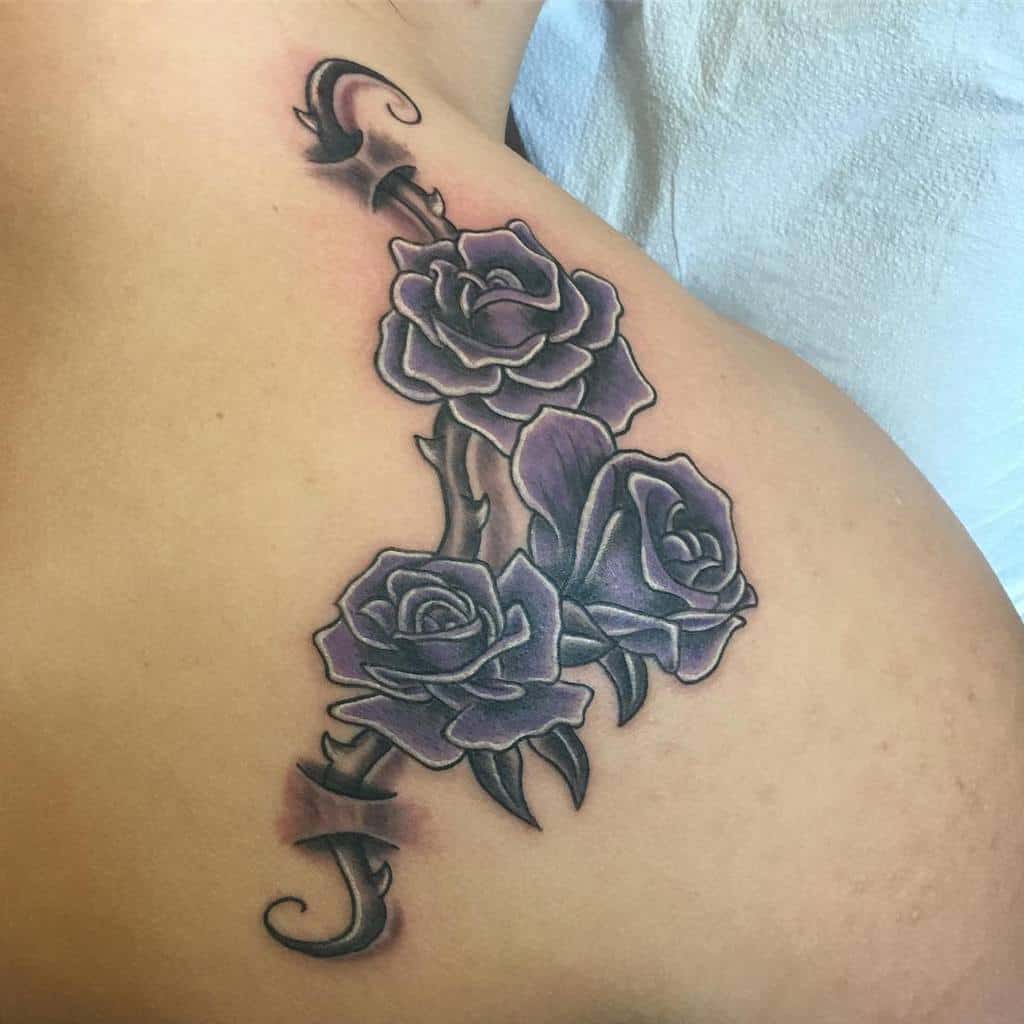 Tattoo of three purple roses with leaves on a shoulder