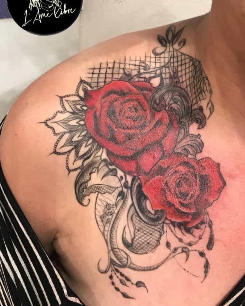 Intricate shoulder tattoo featuring two red roses accented with black lace patterns, swirls, and ornamental detailing for a unique design