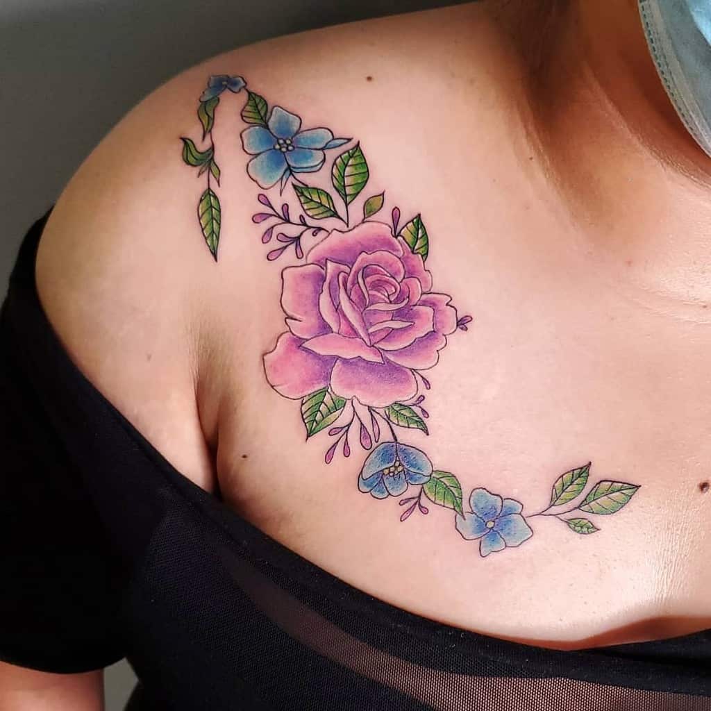 Beautiful shoulder tattoo featuring a soft pink rose surrounded by delicate blue flowers and green leaves, creating a vibrant and feminine design