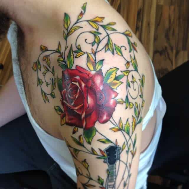 Intricate shoulder tattoo featuring a bold red rose surrounded by swirling vine patterns and golden accents, adding depth and vibrancy to the design
