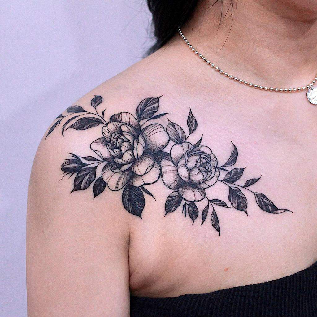 Delicate black and gray shoulder tattoo featuring detailed roses and flowing leaves, creating a soft and timeless floral design