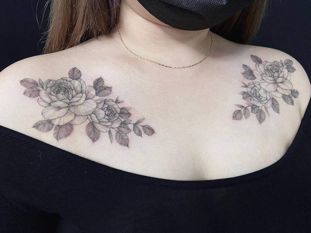 Delicate and symmetrical floral shoulder tattoo featuring intricate line work and shading, creating a soft and elegant design that beautifully frames the collarbone