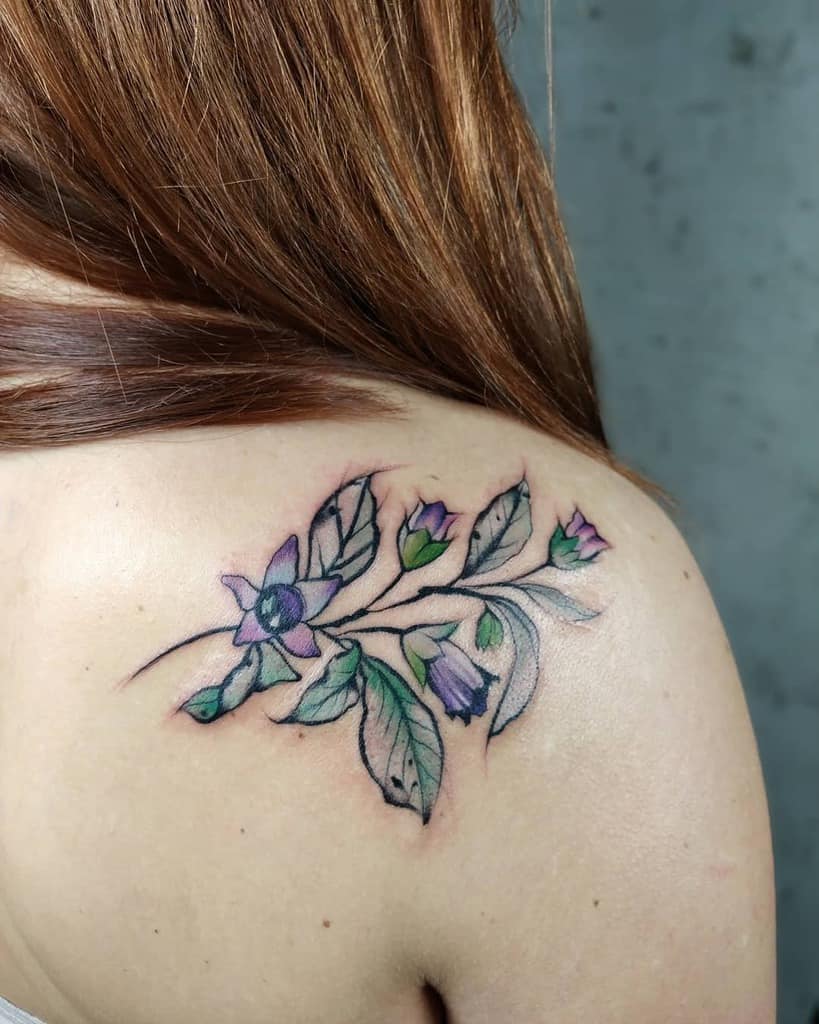 Floral tattoo with purple flowers and green leaves on a shoulder