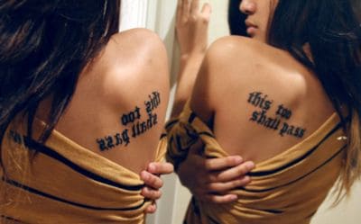 "This Too Shall Pass" tattoo on the upper back, with a second tattoo reading "This too shall pass" on the other side.