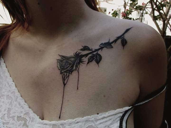 A delicate black and gray tattoo of a rose with dripping ink, placed across the shoulder and collarbone area