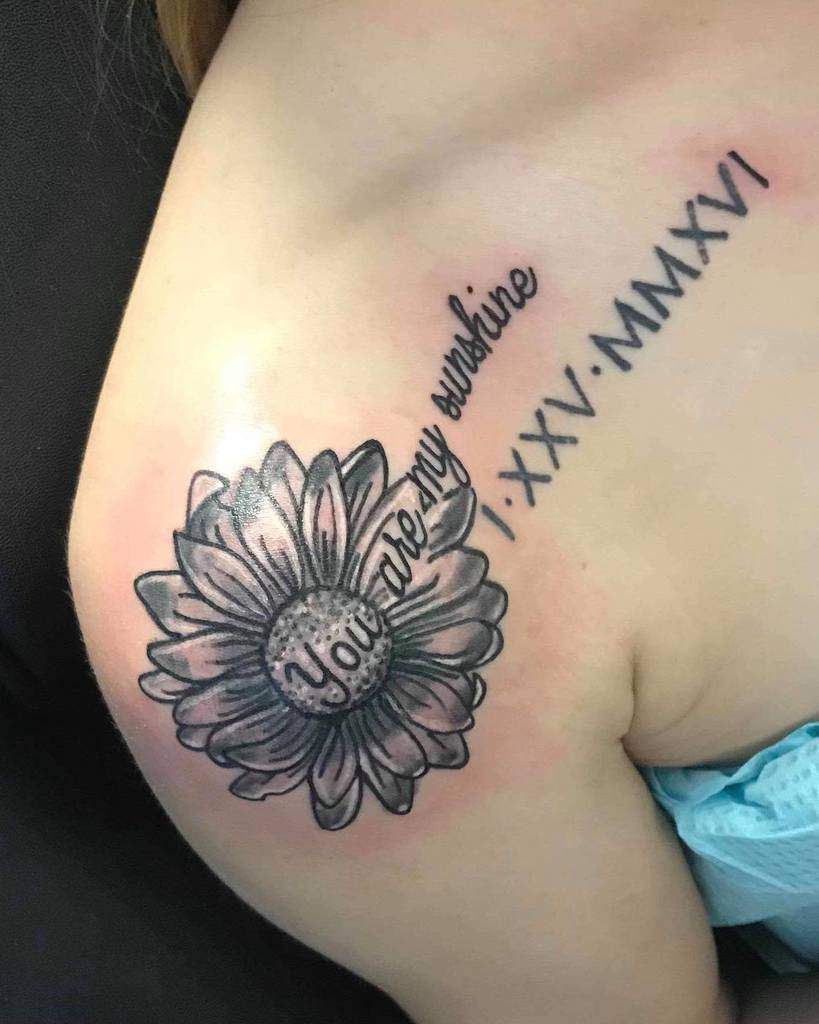 Tattoo of a daisy with "You are my sunshine" and Roman numerals on a shoulder