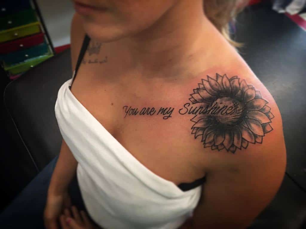 Woman with a sunflower tattoo on her shoulder, text reads "You are my Sunshine"