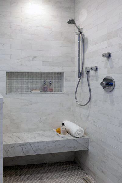 White marble shower with built-in bench, niche shelving, and modern handheld showerhead.