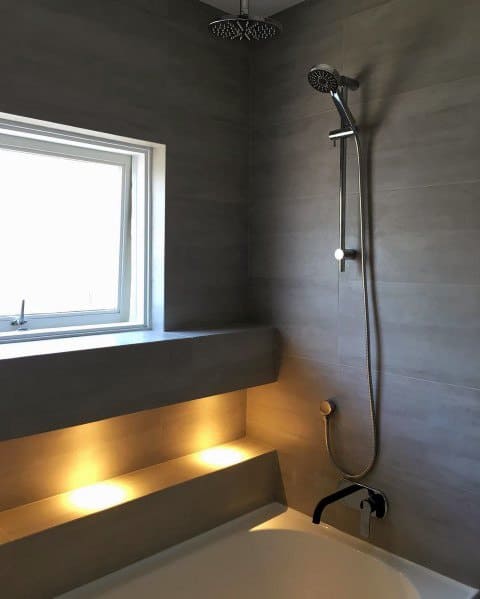 Contemporary shower with a window, sleek gray tiles, and soft LED lighting illuminating the built-in seating for a stylish, airy feel