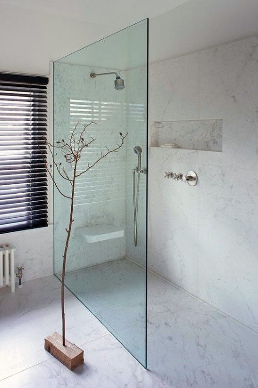 Minimalist shower with glass divider, marble walls, recessed shelf, and natural light.