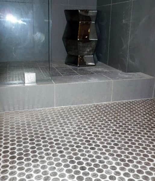 Modern shower with silver penny tile flooring, white grout, and sleek gray tiled walls.
