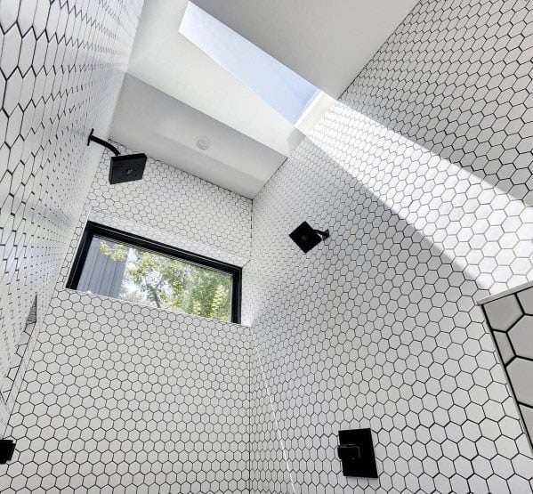Bright shower with white hexagonal tiles, black fixtures, and natural light streaming through a skylight.