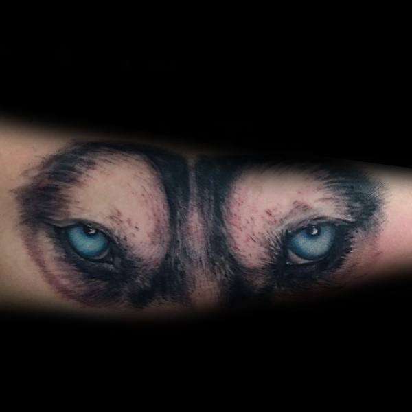 Hyper-realistic Siberian Husky eye tattoo on a man's forearm, featuring piercing blue eyes and detailed fur shading for an intense and striking look.
