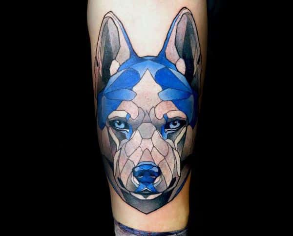 Geometric Siberian Husky tattoo on a man's arm, featuring bold blue tones, sharp angular shapes, and piercing blue eyes for a modern, abstract look.
