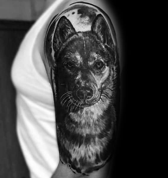 Hyper-realistic black and gray Siberian Husky tattoo on a man's upper arm, featuring intricate fur details and a striking lifelike gaze.