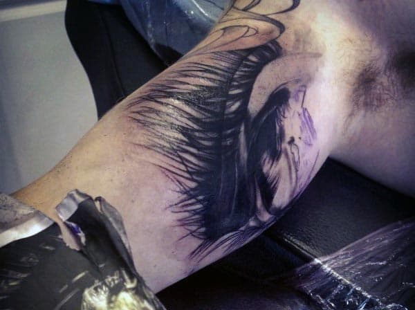 Abstract black and grey tattoo of a distorted eye with intense shading and sharp, jagged lines, creating a dark and surreal effect on the inner bicep