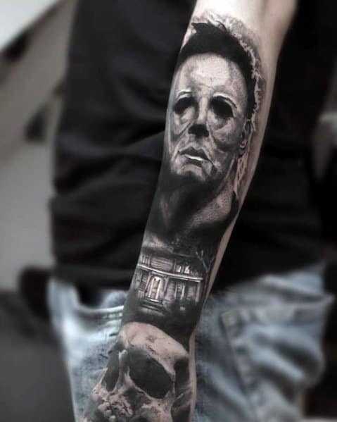 Realistic black and grey Michael Myers tattoo featuring his iconic mask, a haunted house, and a skull for a chilling horror sleeve.