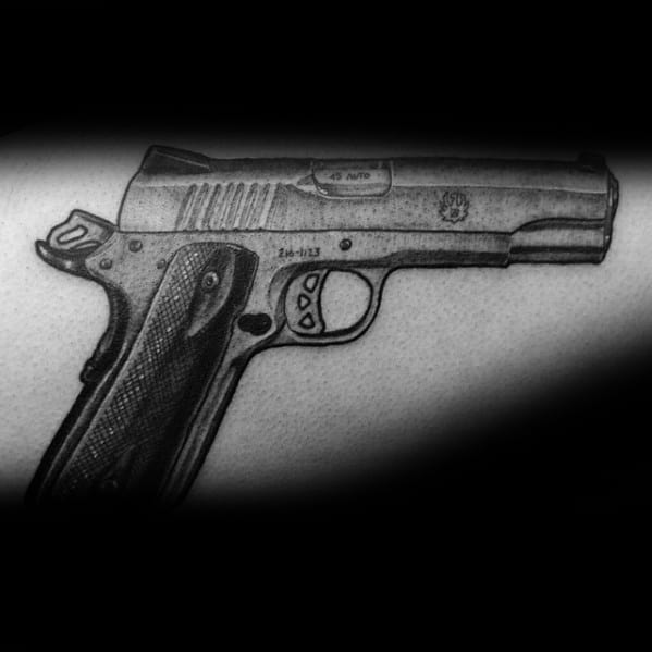 Realistic black and gray tattoo of a 1911 pistol on the arm, featuring fine details, shading, and grip texture for a bold and lifelike effect.