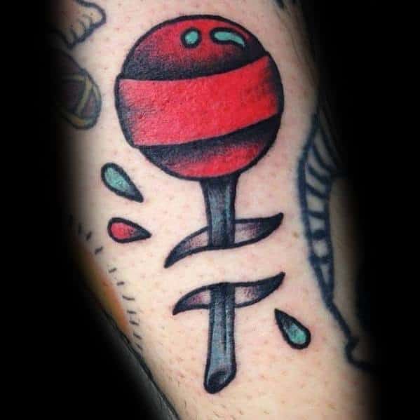 Bold lollipop tattoo with a dagger piercing through it, featuring vibrant red shading and a traditional tattoo style with dynamic details.