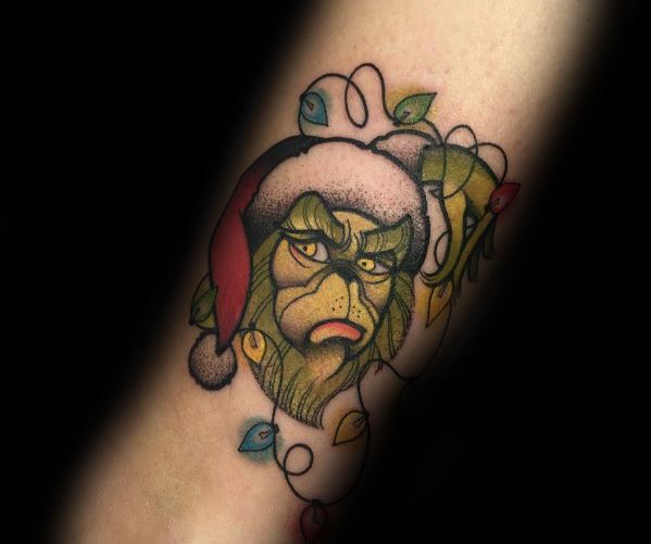Christmas tattoo of the Grinch wearing a Santa hat, wrapped in colorful holiday lights, with a grumpy expression capturing his classic mischievous spirit.