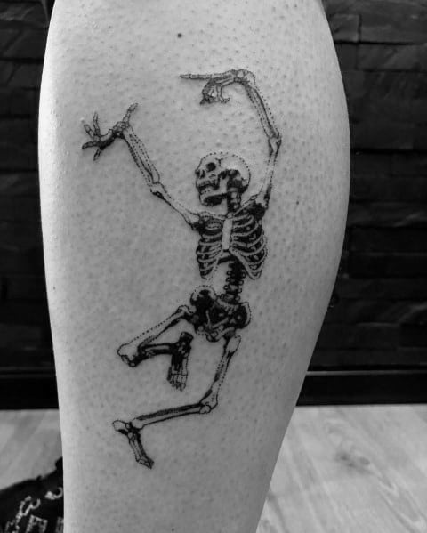 Dancing skeleton tattoo with raised arms and a dynamic pose, inked in bold black for a striking and lively design on the leg.