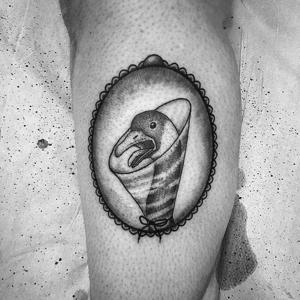 Black and gray tattoo of a goose wrapped in a swaddle, framed within an ornate oval border, inked with fine shading for a vintage-style look.