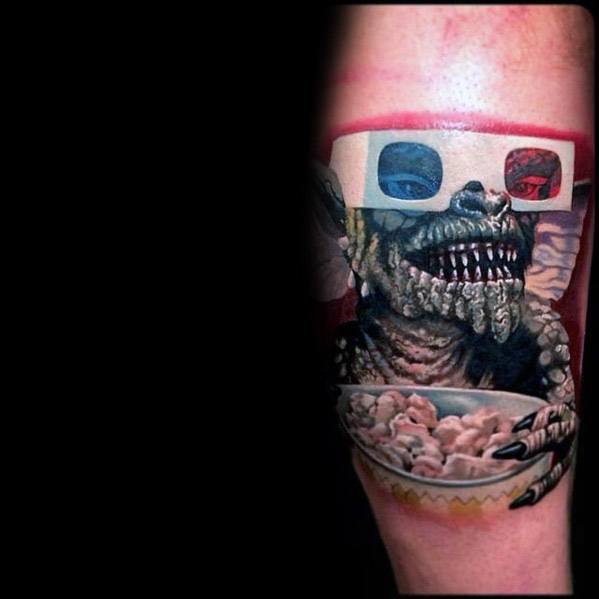 Realistic Gremlin tattoo with 3D glasses, sharp teeth, and a bowl of popcorn, blending horror and nostalgia in vivid detail.