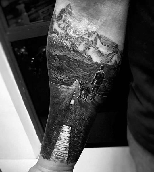 Realistic black and white tattoo of a traveler walking with a dog on an open road toward towering mountains, symbolizing adventure and freedom.