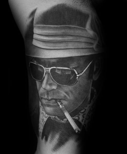 Black and white Hunter S. Thompson tattoo featuring a highly detailed portrait with aviator glasses, a bucket hat, a cigarette, and bold shading for realism.