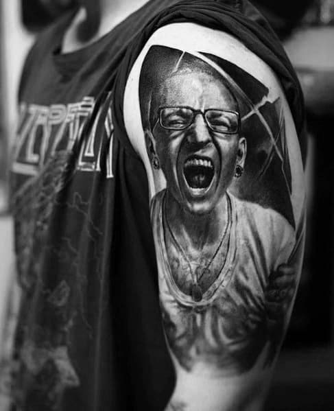Black and gray tattoo of Chester Bennington screaming, with intense shading and a cracked glass effect on the upper arm.