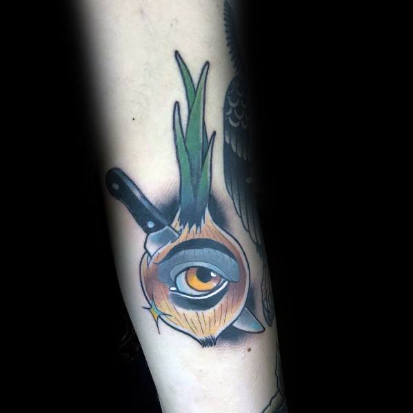Surreal tattoo of an onion with a realistic eye in the center, sprouting green leaves, and a knife embedded in it, blending bold colors with fine details.