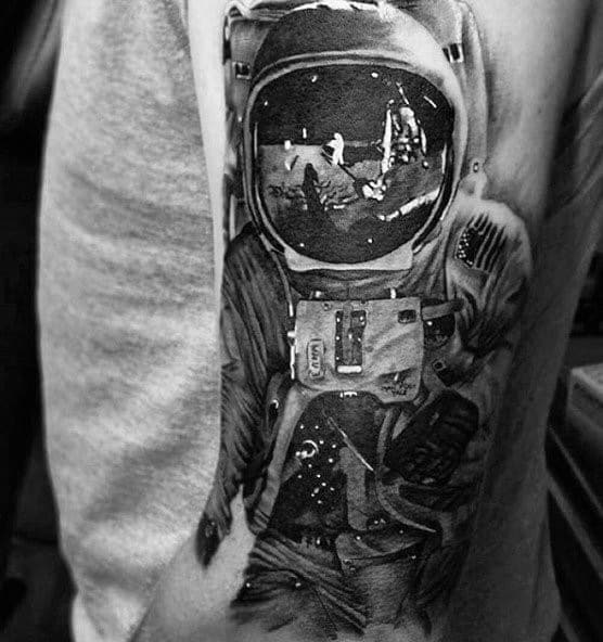 Tattoo of an astronaut with a moon landing scene reflected in the helmet, featuring intricate shading and realism for a bold space-themed design.