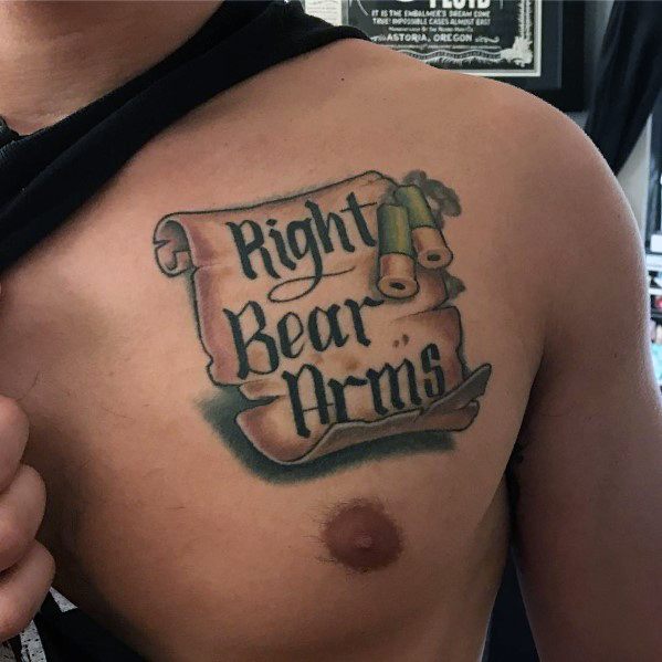 Chest tattoo featuring a parchment scroll with "Right to Bear Arms" in bold script, accompanied by two shotgun shells for a strong statement design.