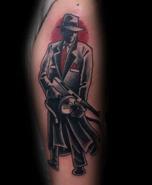 Classic neo-traditional gangster tattoo featuring a suited mobster holding a Tommy gun, with bold black outlines, red accents, and a vintage crime aesthetic.