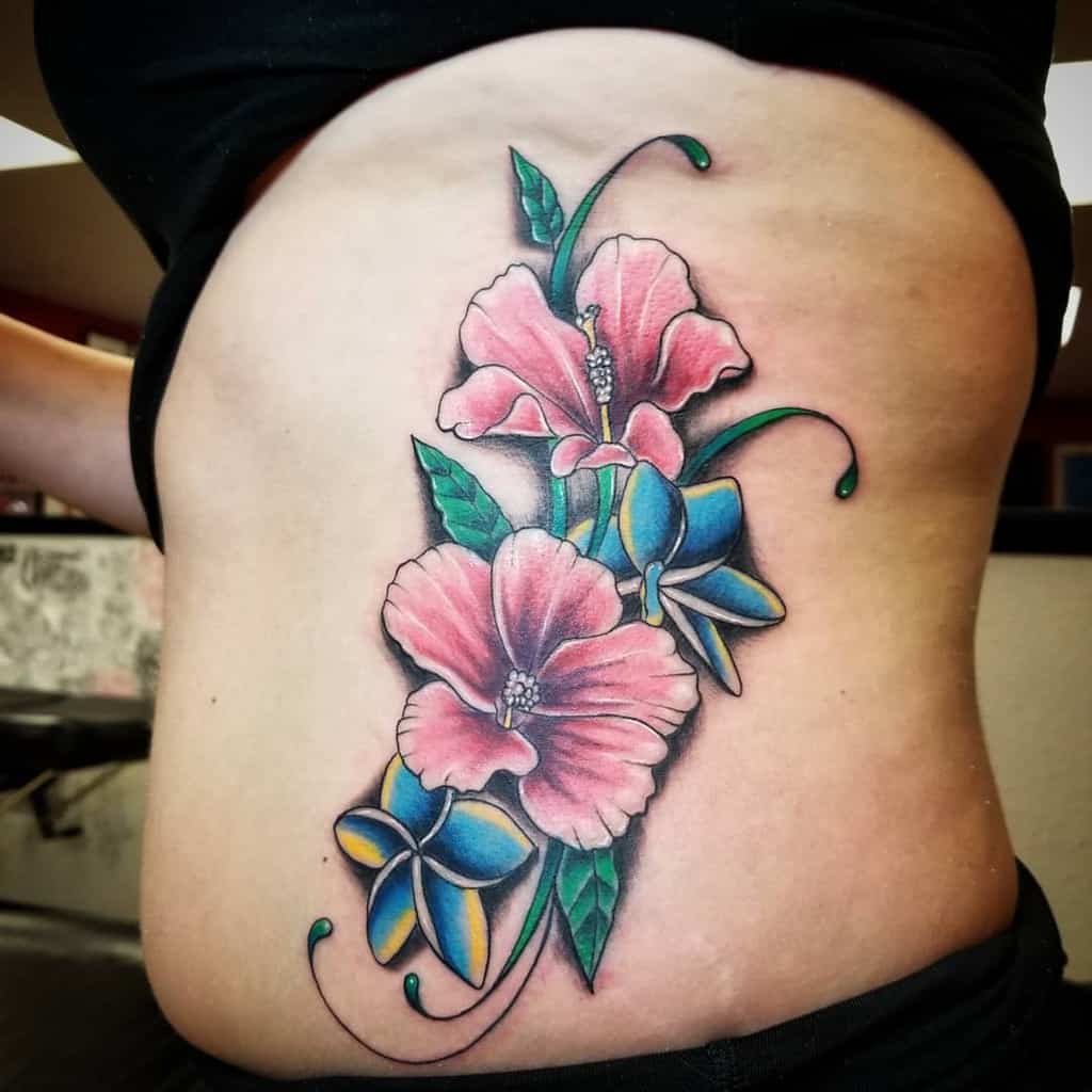 Colorful plumeria flower tattoo on a woman's side