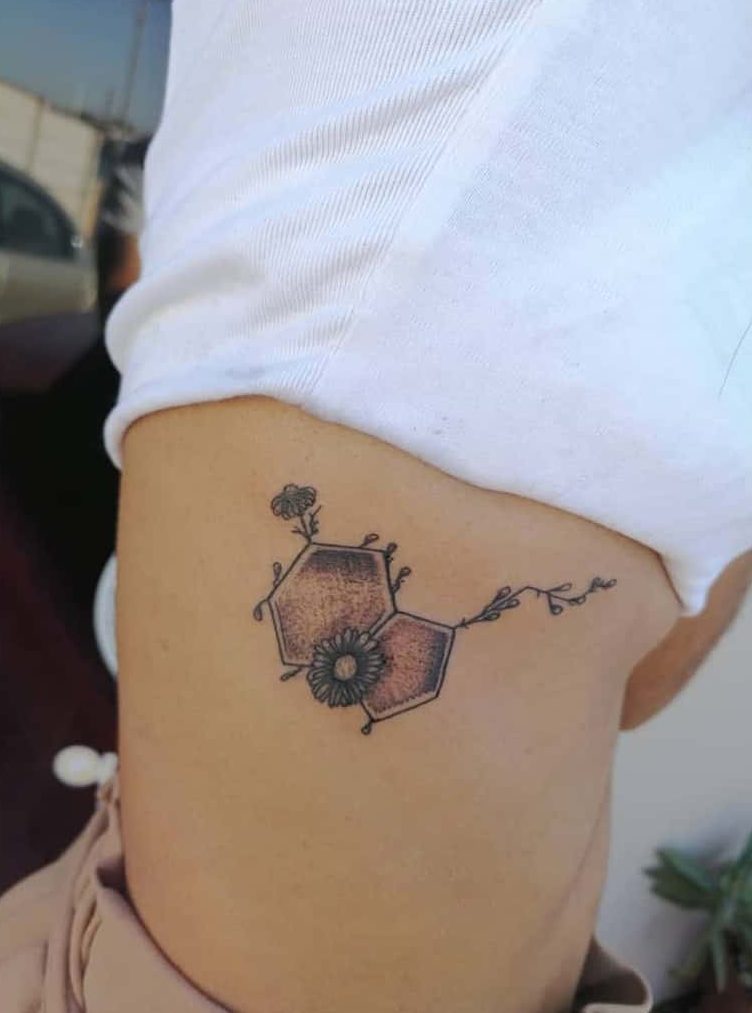 A delicate tattoo of the serotonin molecule intertwined with blossoming flowers graces a person's side