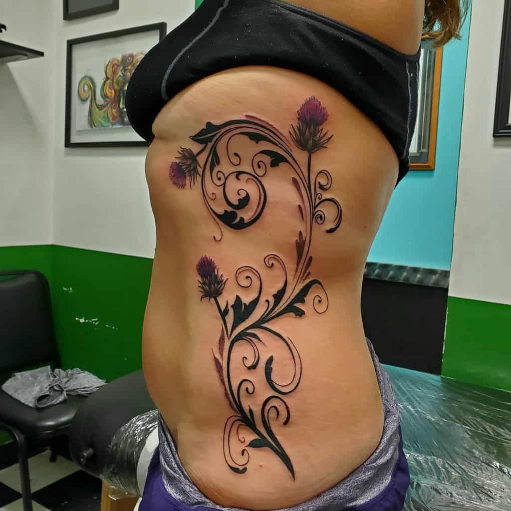 Elegant side tattoo featuring purple thistle flowers intertwined with intricate black swirling vines