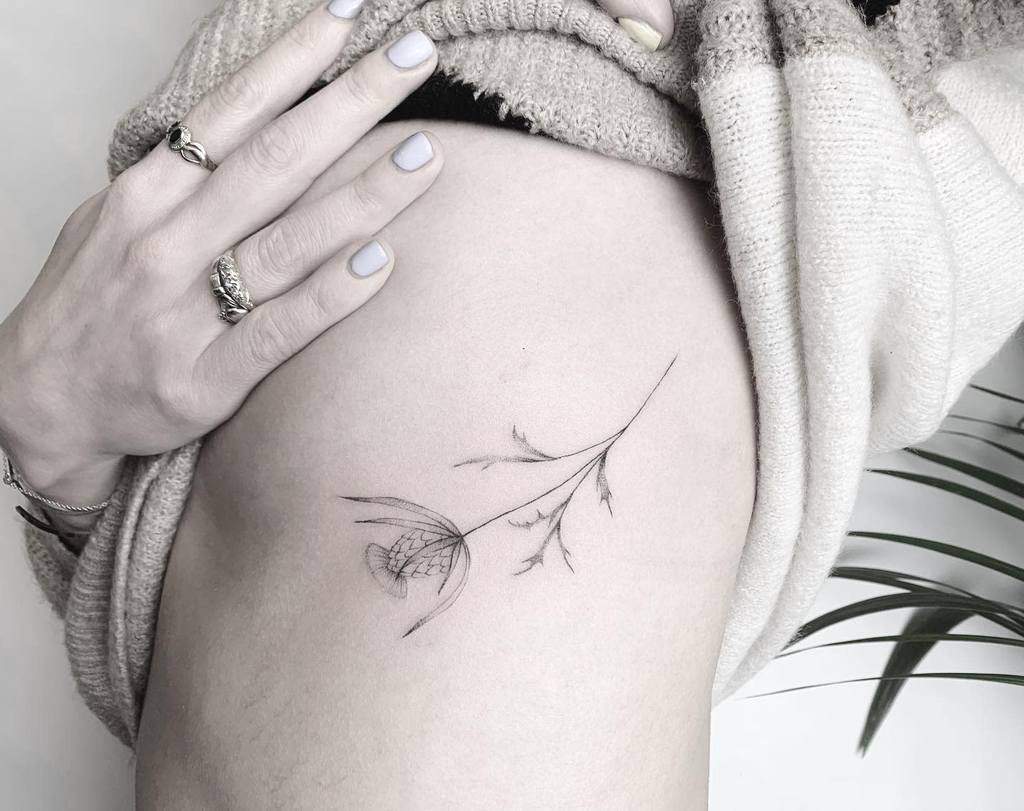 Elegant and minimalistic side tattoo of a single thistle stem with fine, delicate linework