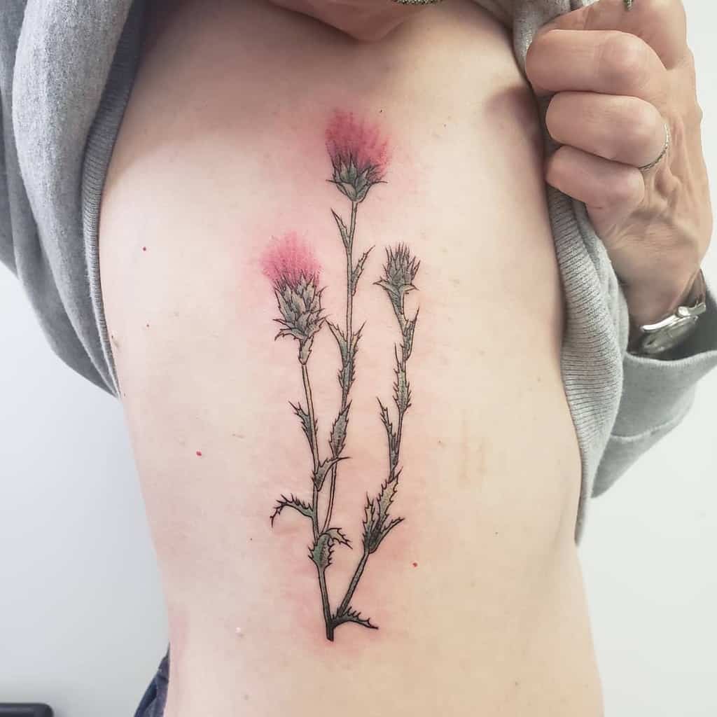A person reveals a stunning side tattoo adorned with thistle flowers, beautifully highlighted with pink accents