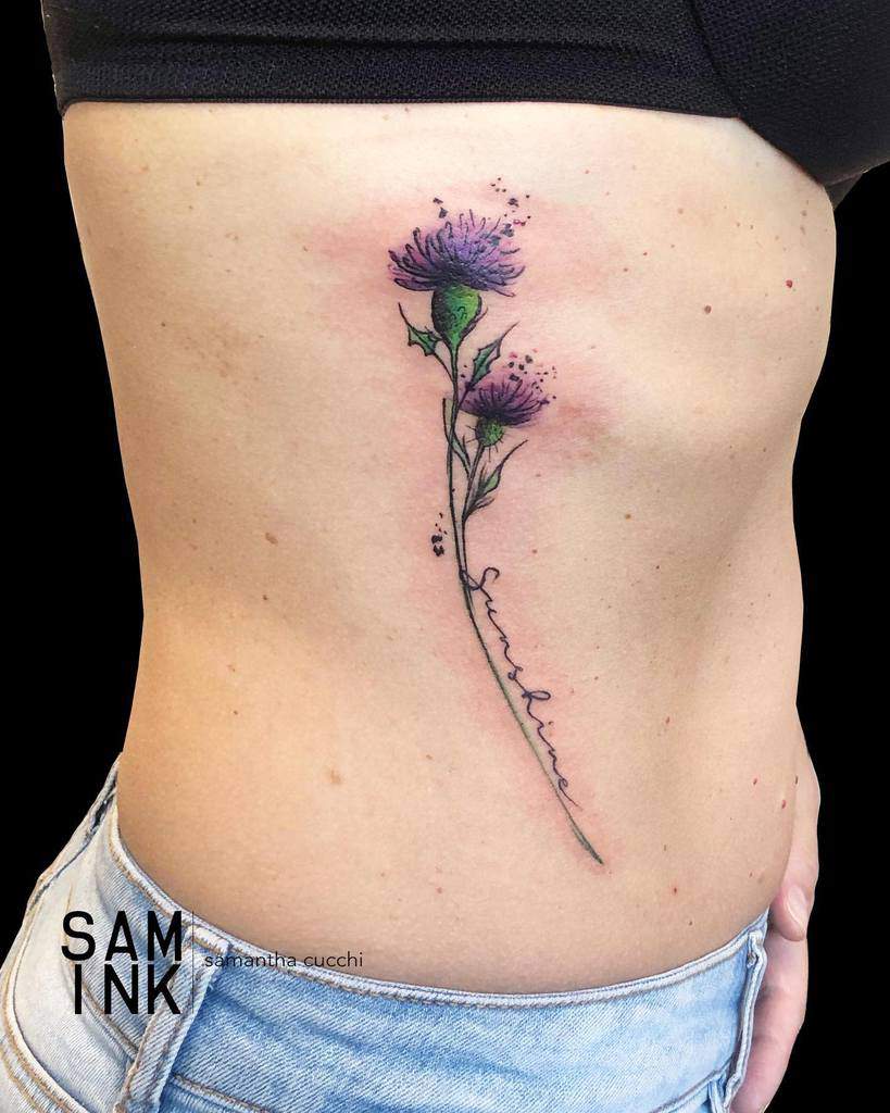 Rib tattoo featuring two delicate purple thistles, their thin stems gracefully intertwined with elegant cursive writing