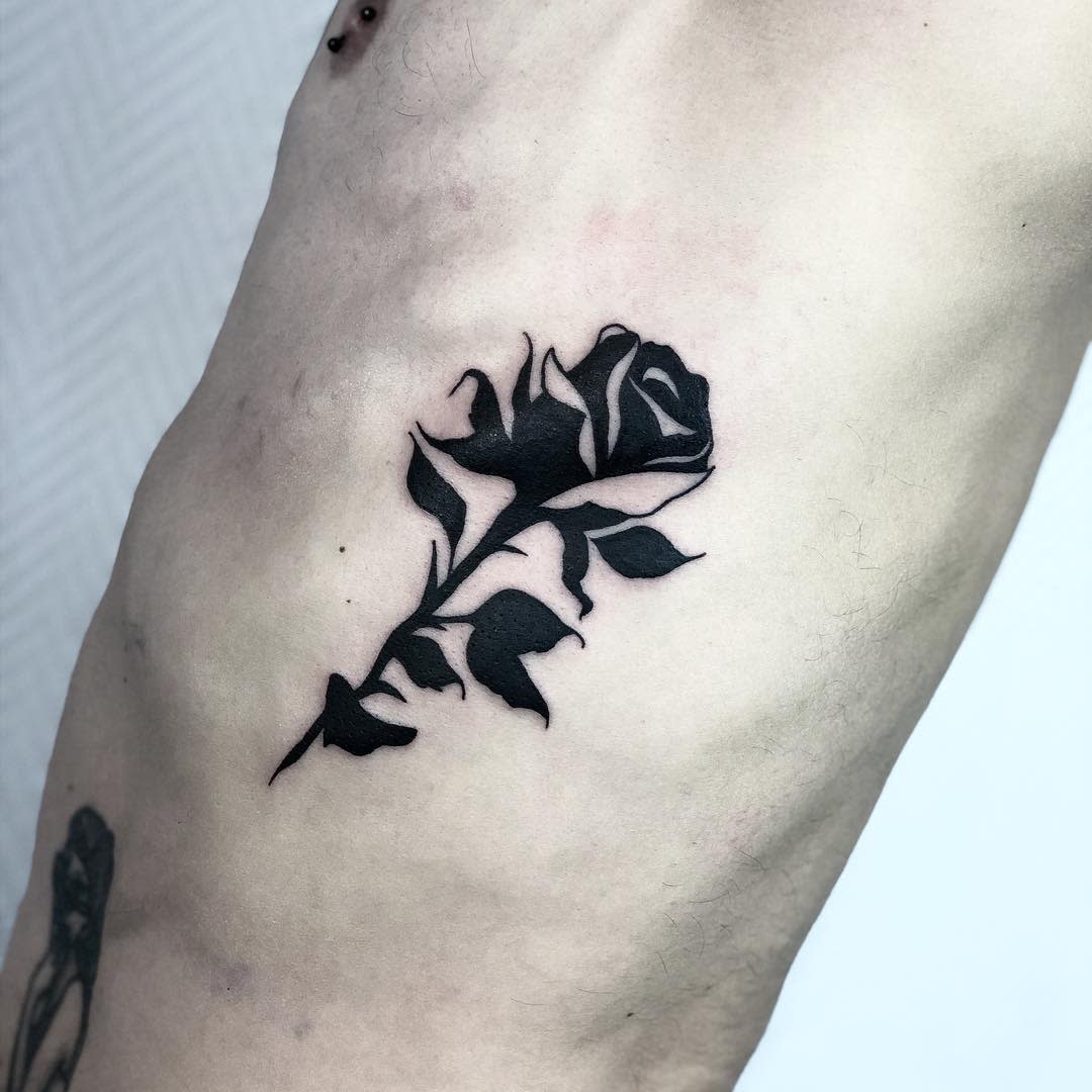 A single elegant black rose tattoo graces a man's side