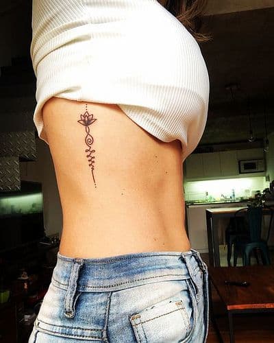 Unalome tattoo with a lotus on the ribcage, symbolizing spiritual growth, enlightenment, and the journey to inner peace.