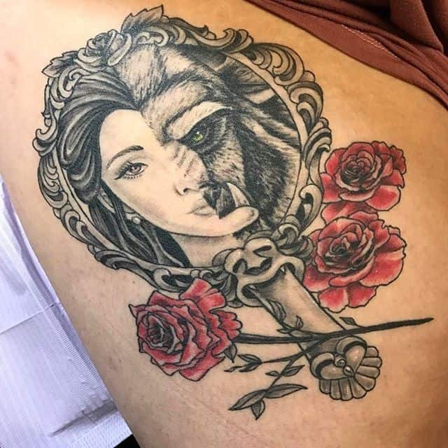 Intricate tattoo of a split-face design featuring Belle and the Beast within an ornate mirror frame, accented with red roses and a key.
