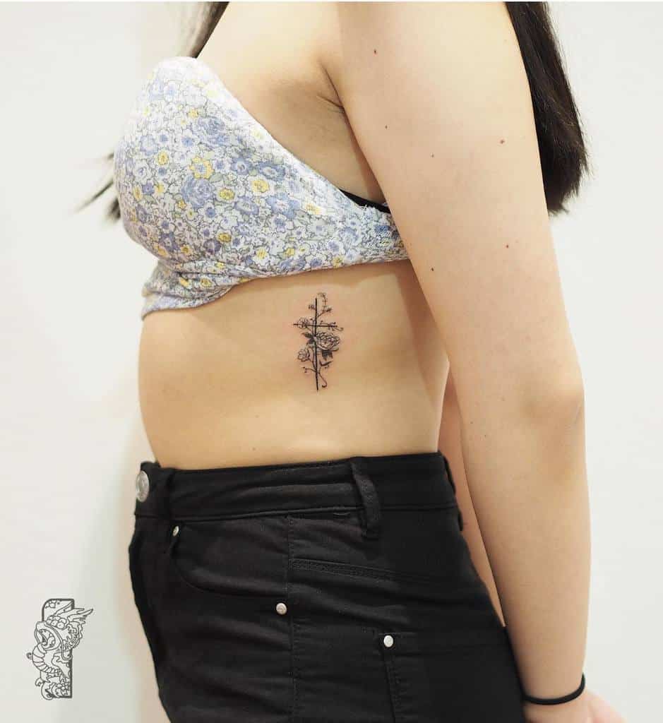 Woman with floral tattoo on left ribcage and a delicate cross pendant