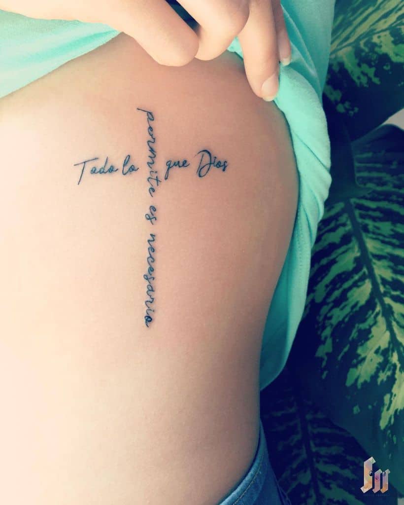 A beautifully inked script tattoo of a cross gracefully adorns the skin, with the words "Todo lo que Dios permite es necesario,